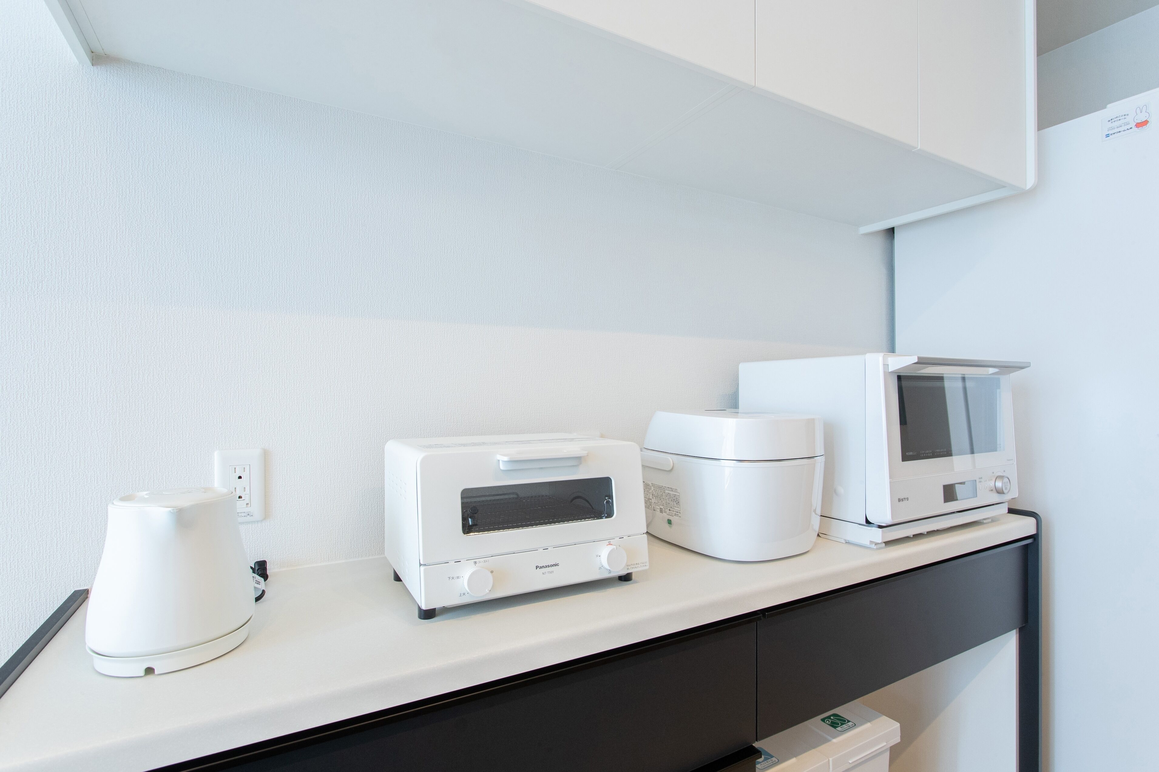 A kitchenette with a microwave, toaster, and coffee maker on a white countertop.
