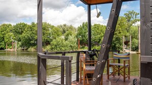 Une terrasse en bois avec une chaise et une table, donnant sur une étendue d’eau et des arbres.