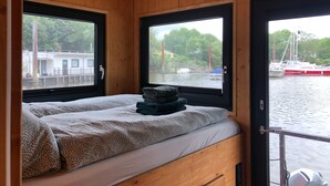 Une cabine avec un lit, une fenêtre et une vue sur les bateaux qui naviguent.