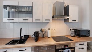 Eine moderne Küche mit weißen Schränken, einer Edelstahl-Dunstabzugshaube, einem integrierten Geschirrspüler und einer Kaffeemaschine.
