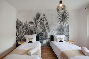A room with two beds, a woven headboard, a round wooden side table, a hanging light fixture, and a wall tapestry. - Apartment 'Salvo' with Balcony and Wi-Fi (Mannheim)