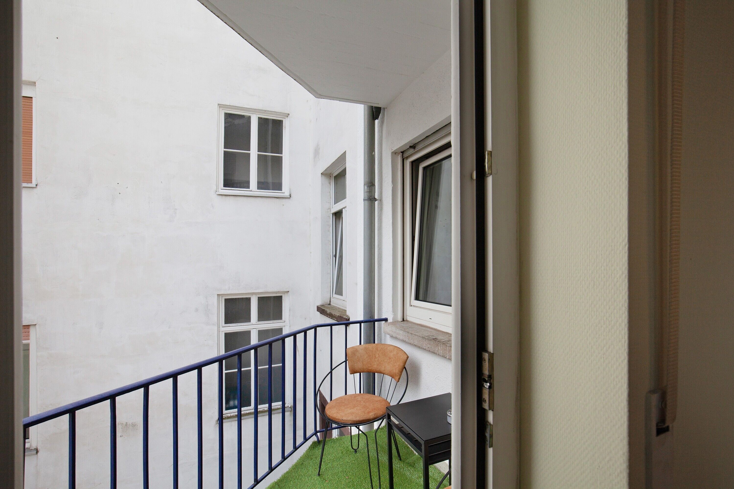 Un balcon avec une chaise et une table, des murs blancs et une fenêtre.