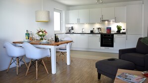 Eine moderne Küche mit weißen Schränken, einem Esstisch mit Stühlen und einem grauen Sofa.