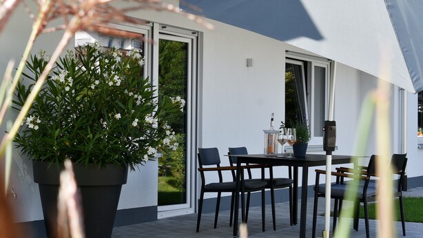 Ein moderner Essbereich im Freien mit Tisch und Stühlen, einem Blumentopf und einem großen Fenster.