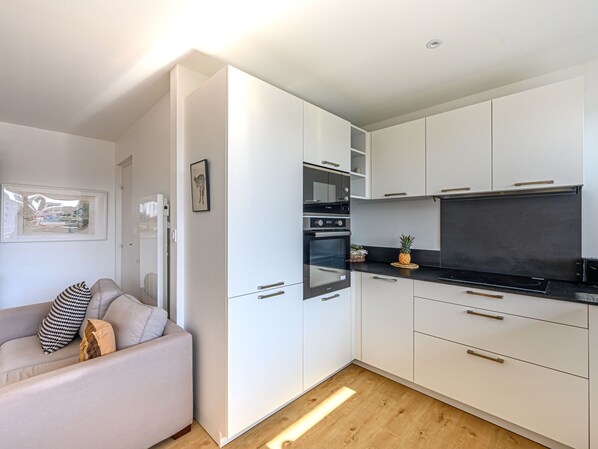 A modern kitchen with white cabinets, a black countertop, and a built-in oven. There is a small island with a pineapple on it.