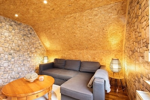 A cozy room with a stone wall, a gray sofa, a wooden table, and a unique lamp.