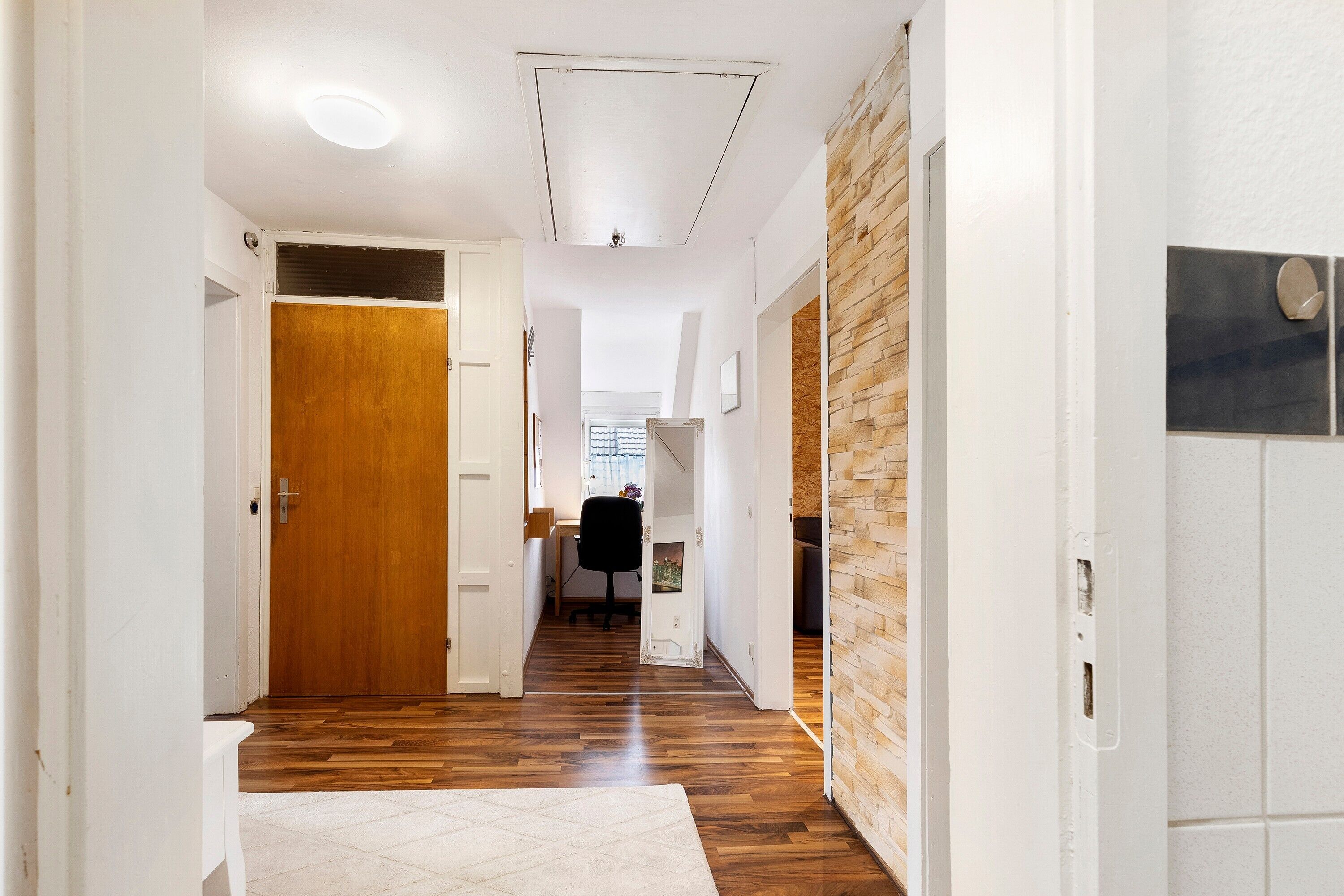 A hallway with wooden flooring, white walls, and a door leading to a room.