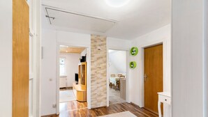 Un pasillo con piso de madera, pared blanca, puerta de madera y una pequeña mesa blanca.
