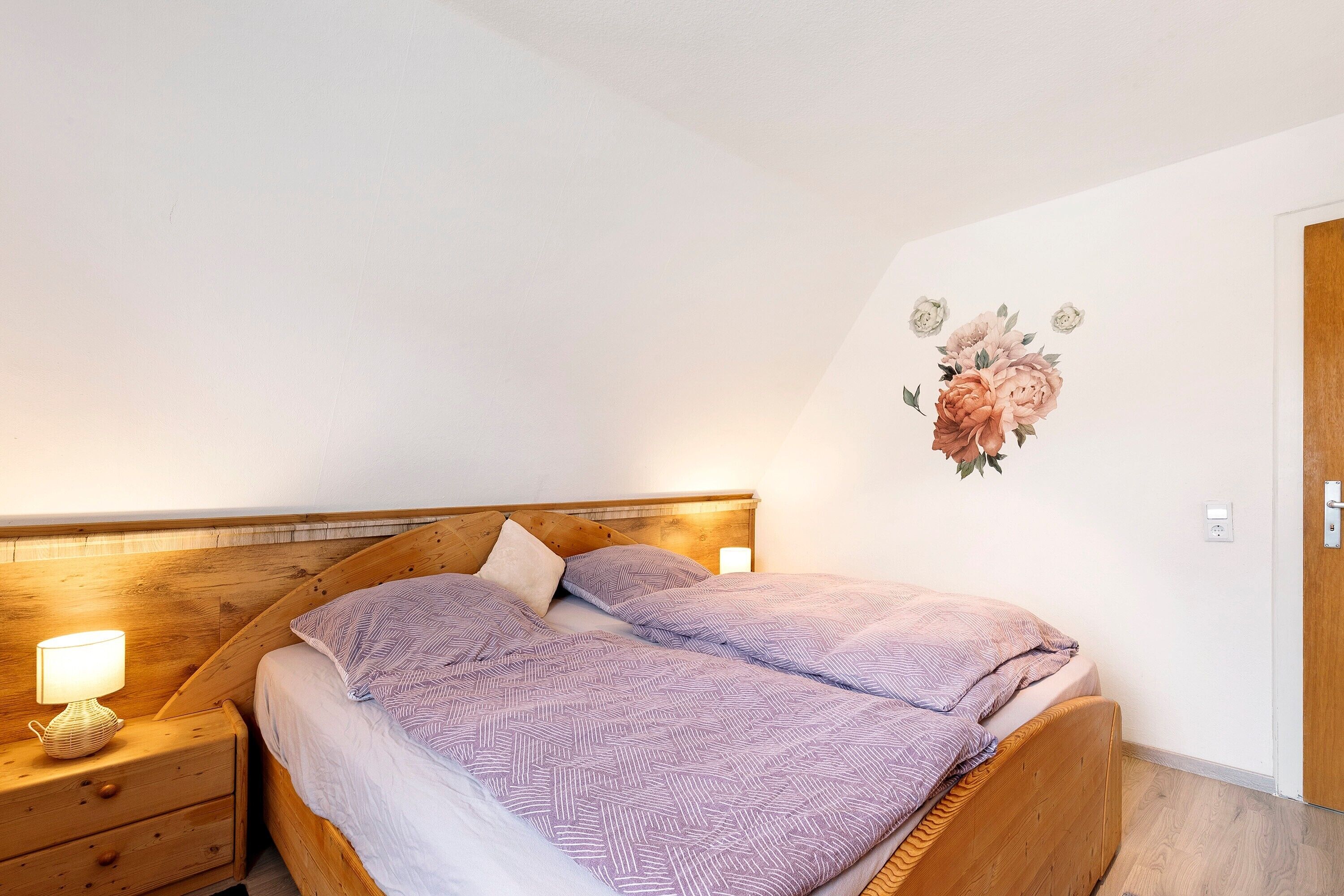 Ein Schlafzimmer mit hölzernem Kopfende, einem Nachttisch mit Lampe und einer Wanddekoration mit Blumenmuster.