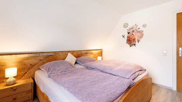 Un dormitorio con cabecera de madera, mesita de noche con lámpara y decoración floral en la pared.