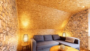 Una habitación acogedora con una pared de piedra, un sofá gris, una mesa redonda de madera y una lámpara de pie.