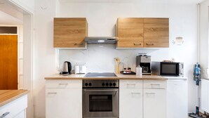 Una cocina compacta con armarios blancos, horno empotrado, microondas y cafetera.