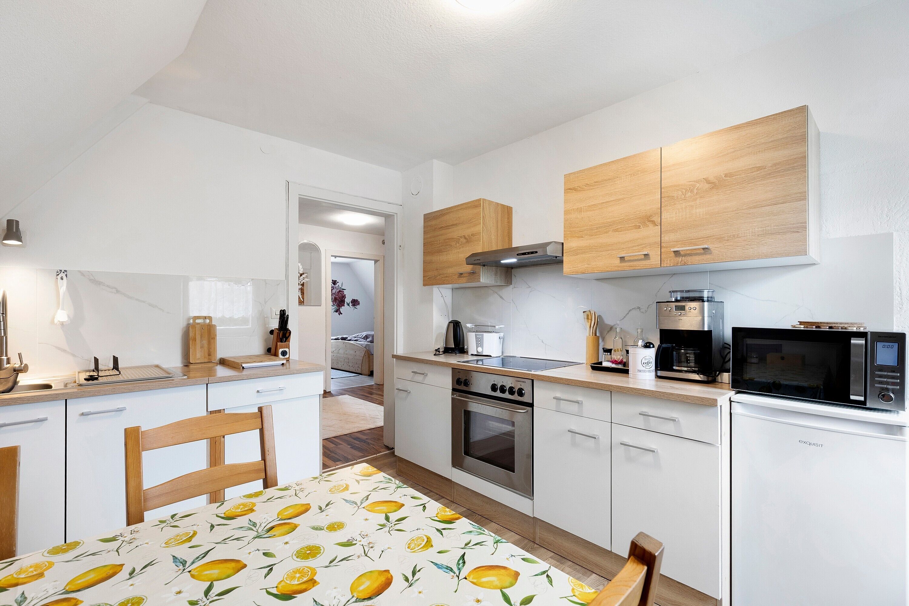 A modern kitchen with white cabinets, a built-in oven, microwave, and coffee maker.