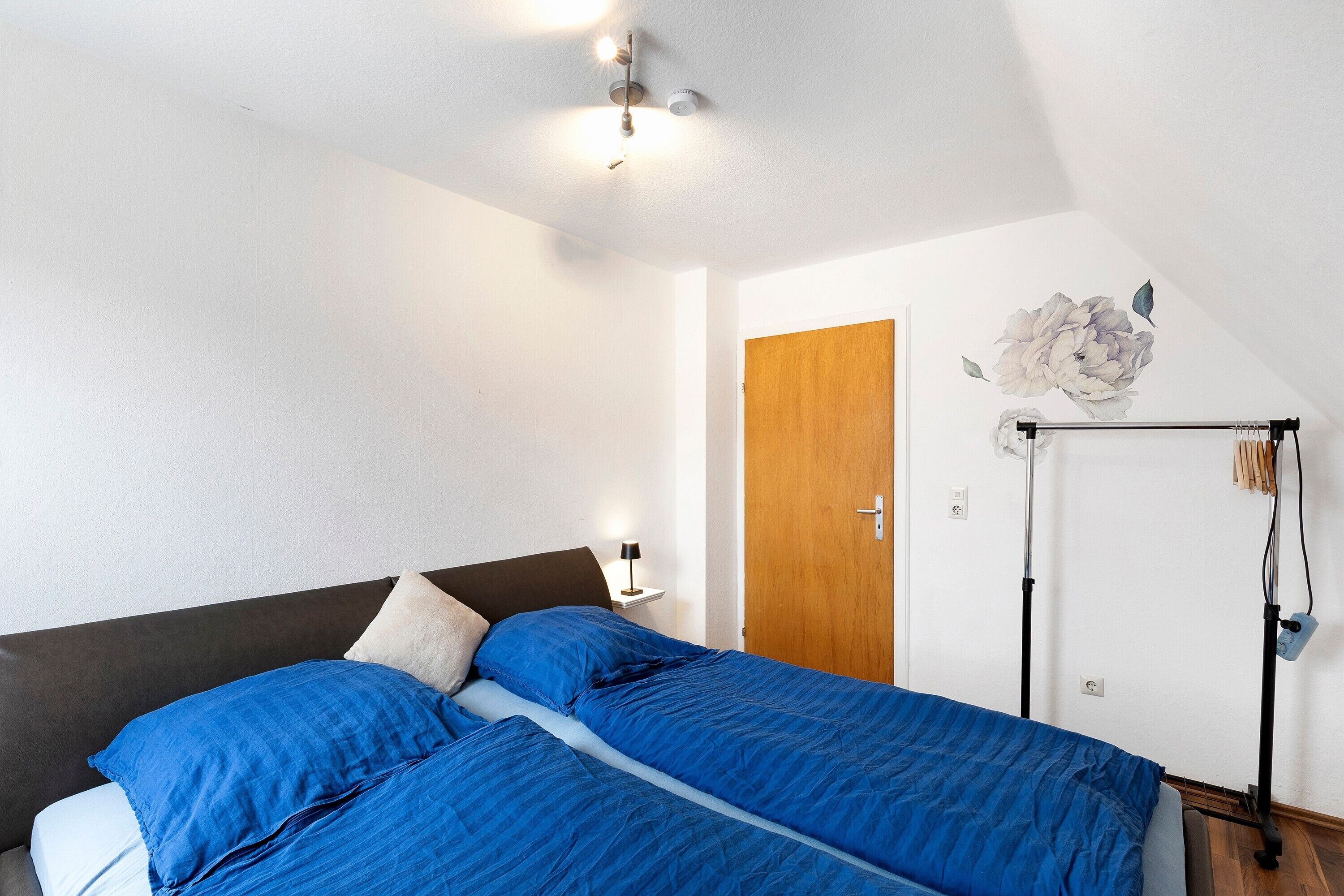 A bedroom with a bed, a nightstand, a ceiling fan, a wooden door, and a wall-mounted radiator.
