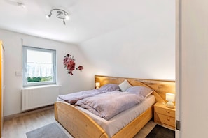 A bedroom with a wooden bed, a window, a radiator, and a nightstand with a lamp.