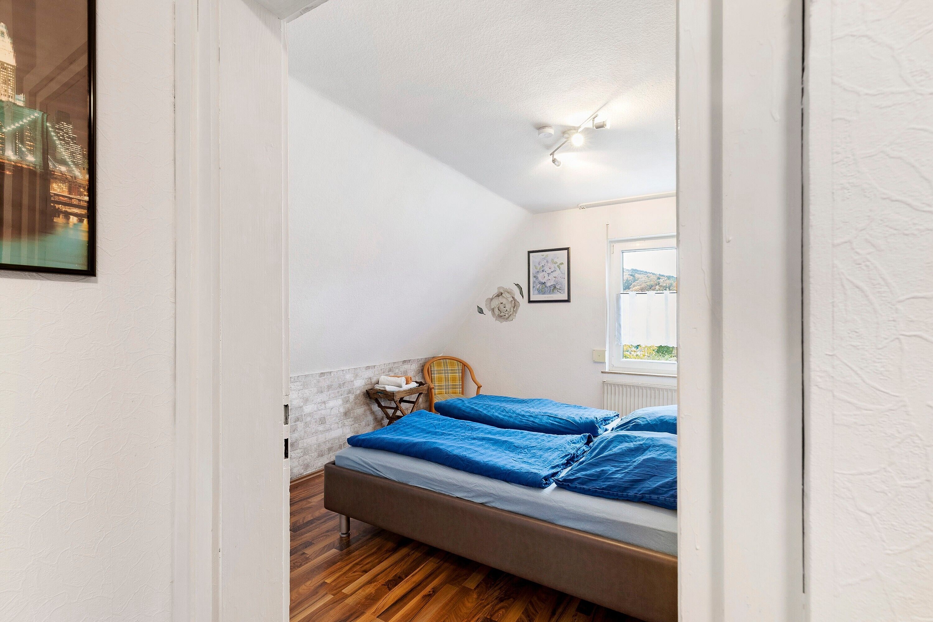 Un dormitorio con cama, una silla, un cuadro en la pared y una ventana con vistas.