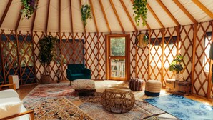 L’intérieur chaleureux d’une yourte, avec un mur en treillis de bois, un fauteuil vert, un tabouret en osier et un tapis à motifs.