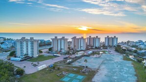Un ensemble immobilier résidentiel de grande hauteur, composé de plusieurs étages, comprenant un espace de stationnement et offrant une vue sur l’océan au coucher du soleil.