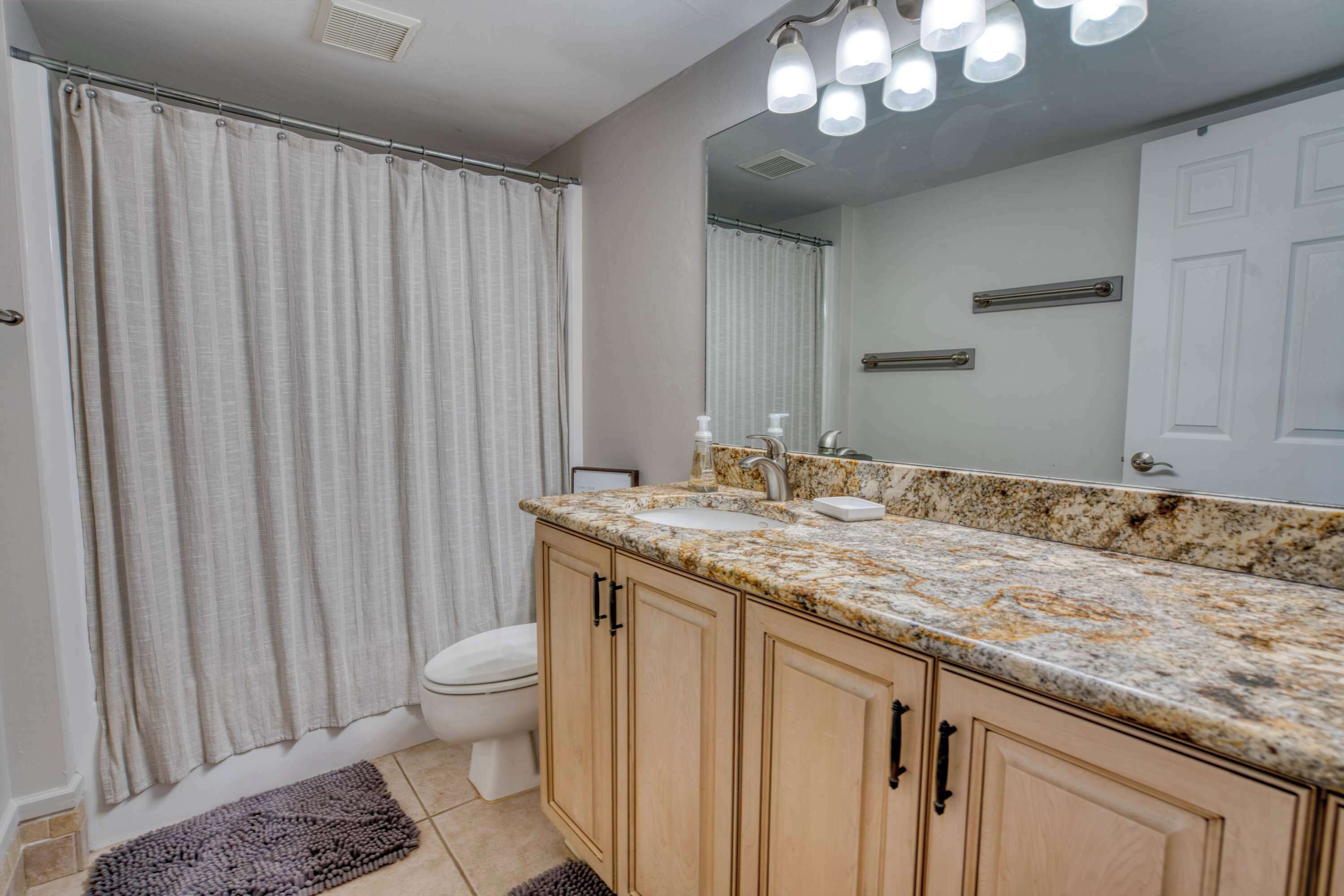 A bathroom with a shower curtain, toilet, sink, and mirror.