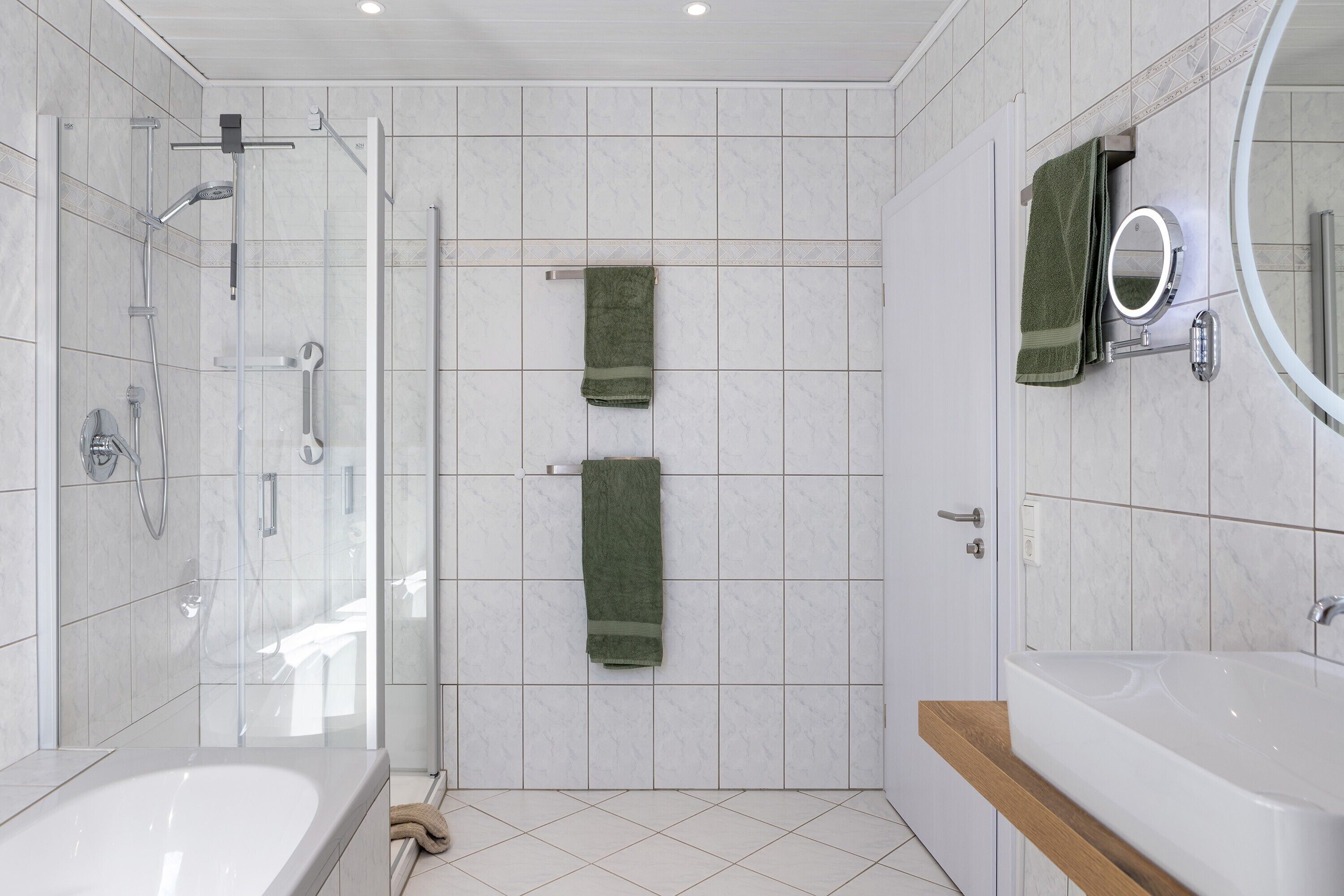 Ein modernes Badezimmer mit einer gläsernen Duschkabine, einer großzügigen Badewanne und einem Spiegel mit runder Rahmung.