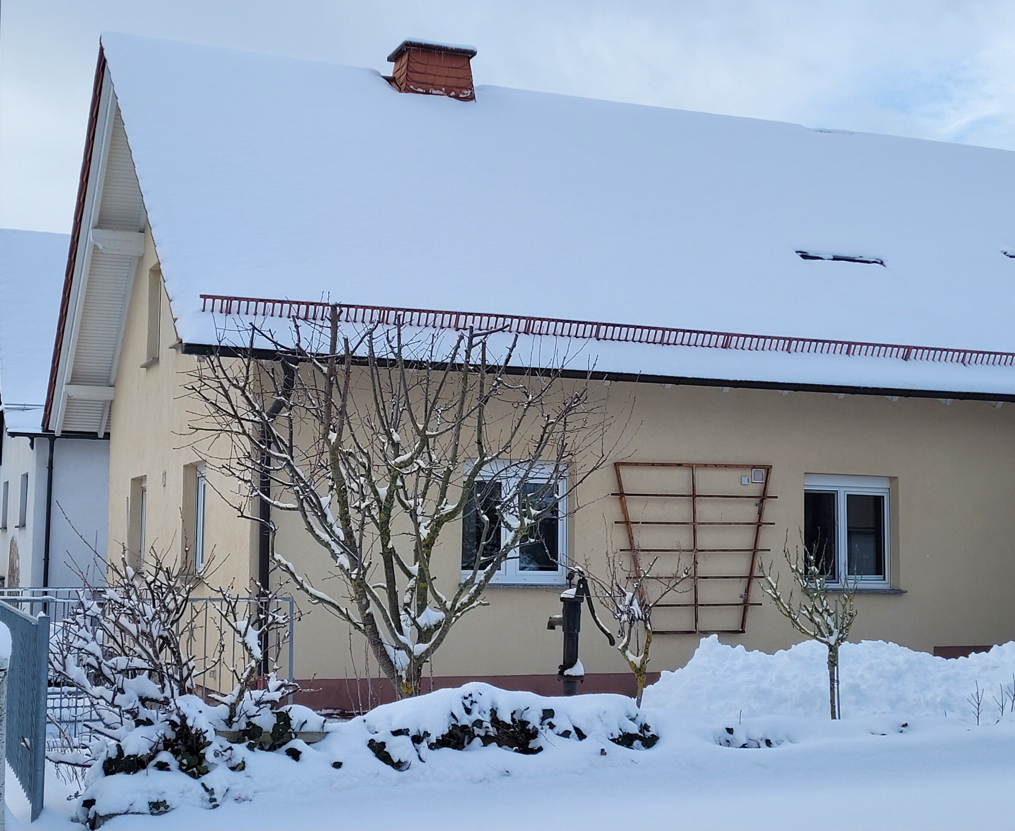 Ein Wohngebäude mit Satteldach, Schornstein und einem Fenster mit einer Metalldachveranda.