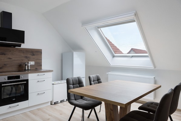 A modern kitchen with a skylight, a dining area with a wooden table and chairs, and a built-in oven.