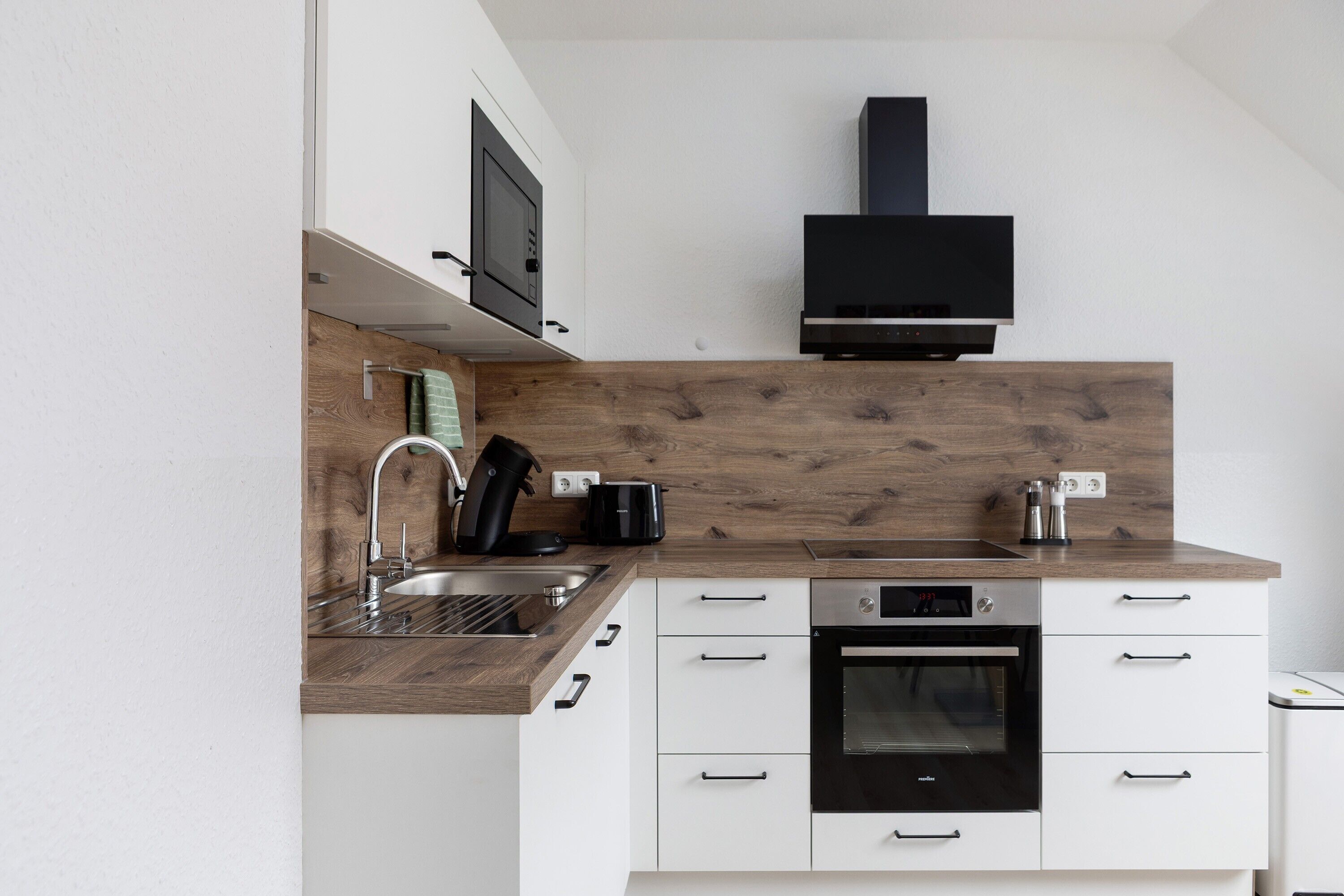 A modern kitchen with white cabinetry, a wooden backsplash, a built-in oven, and a black range hood.