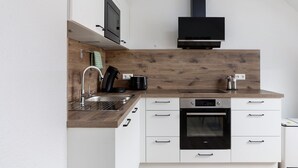 A modern kitchen with white cabinetry, a wooden backsplash, a built-in oven, and a black range hood. - Rhön-Kutscher Apartment with Mountain View, Terrace and Wi-Fi (36419 Buttlar)