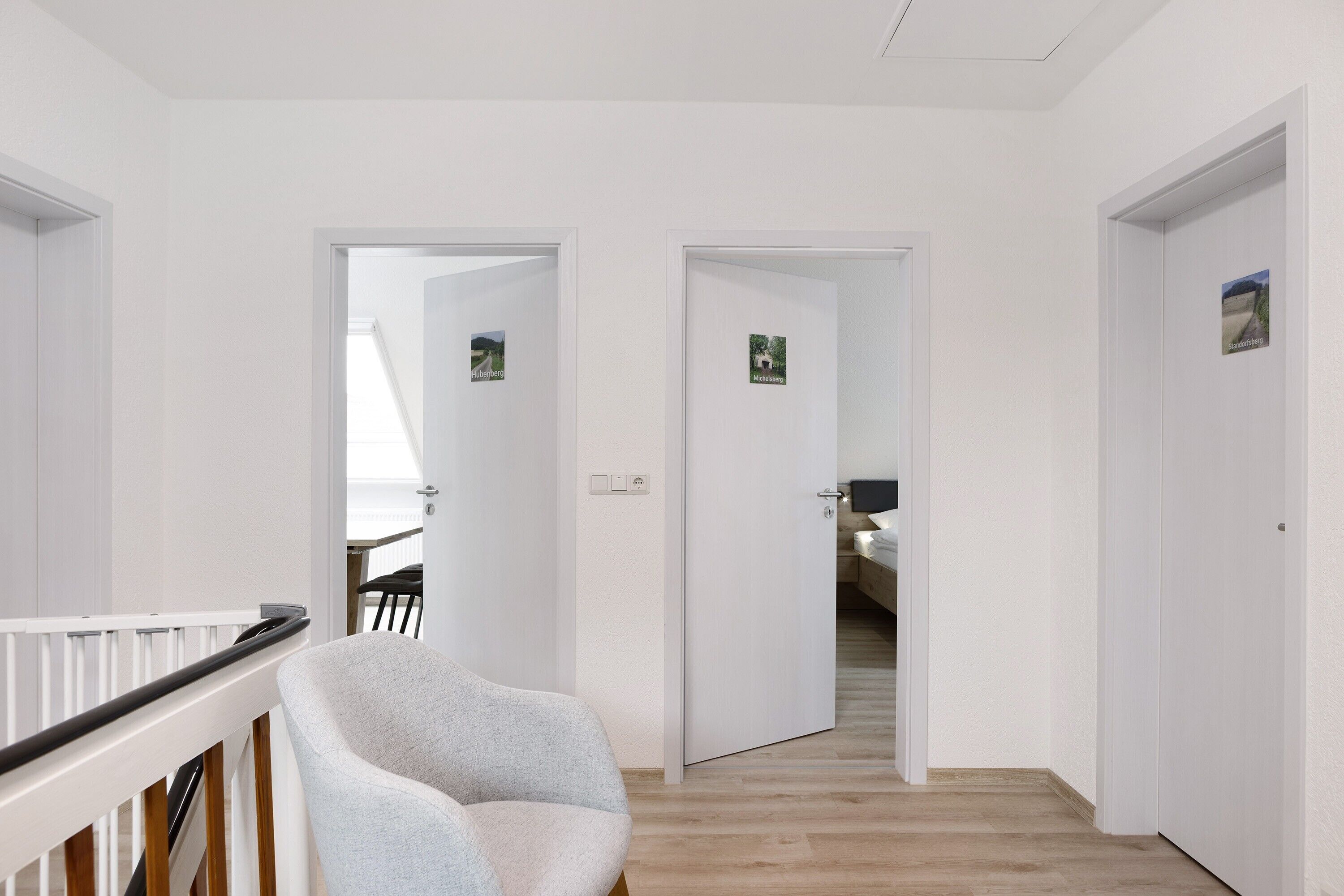 A hallway with white walls, a wooden floor, and a white chair. There are doors leading to other rooms.