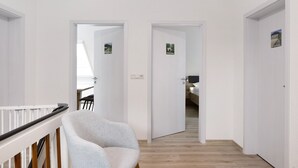 A hallway with white walls, a wooden floor, and a white chair. There are doors leading to other rooms. - Rhön-Kutscher Apartment with Mountain View, Terrace and Wi-Fi (36419 Buttlar)