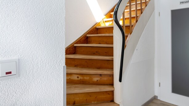 A wooden staircase with a black handrail, white walls, and a visible light switch. - Rhön-Kutscher Apartment with Mountain View, Terrace and Wi-Fi (36419 Buttlar)