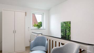 Een kamer met een witte garderobe, een klein tafeltje, twee stoelen, een raam met uitzicht op bomen en een schilderij aan de muur.