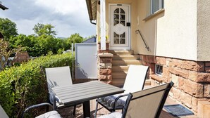 A patio with a table and chairs, a door, and a stone wall. - Rhön-Kutscher Apartment with Mountain View, Terrace and Wi-Fi (36419 Buttlar)