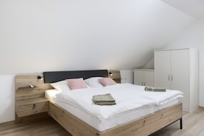 A bedroom with a wooden bed, white bedding, a nightstand, a wardrobe, and a slanted ceiling.