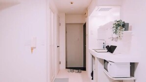 A narrow hallway with a white door at the end, a white sink with a mirror, and a small plant on the counter. - Minimalist Loft 403 (Osaka)