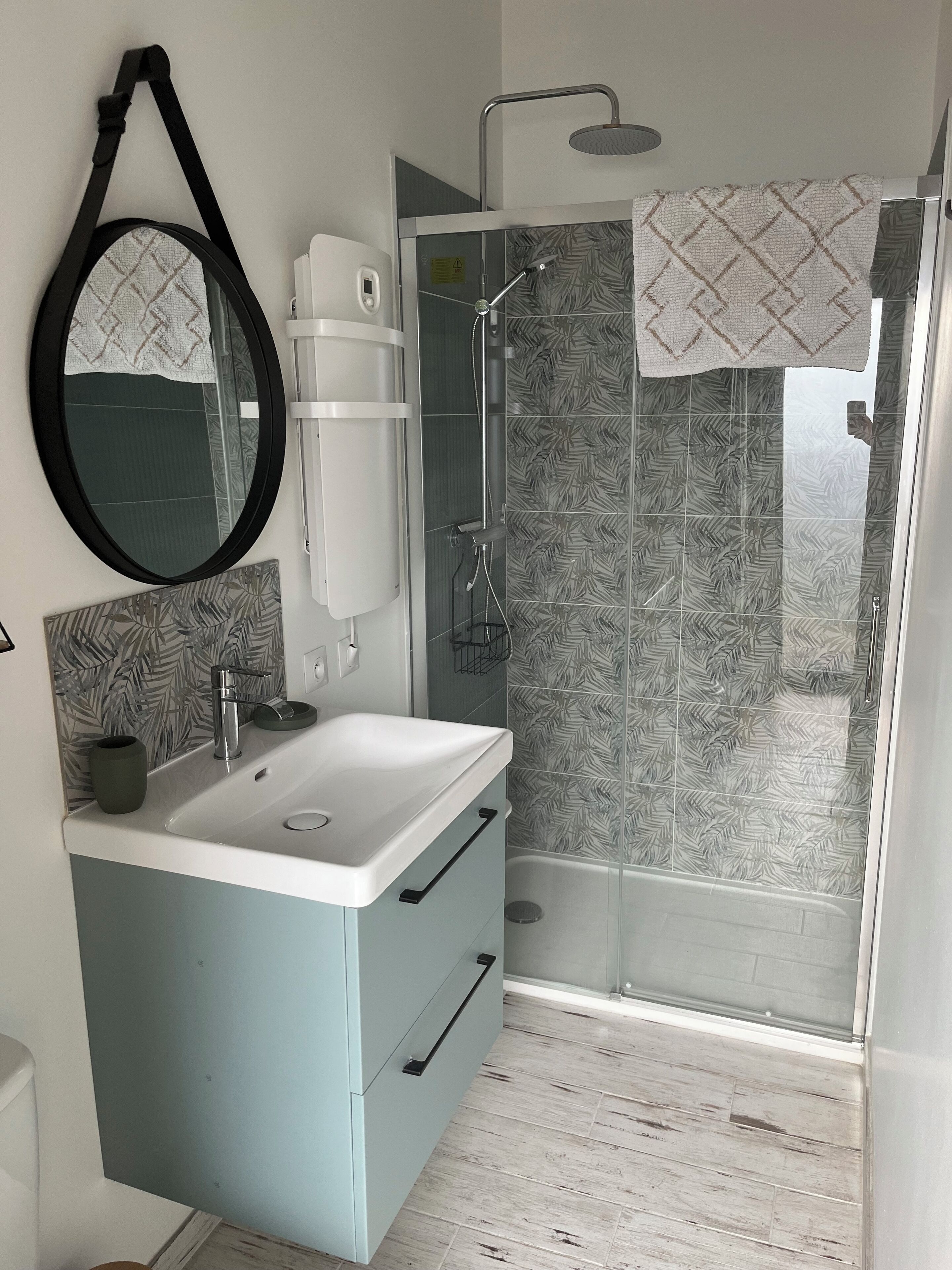 Une salle de bain moderne avec un lavabo blanc, un miroir à cadre noir, une douche avec une porte en verre et des carreaux à motifs.