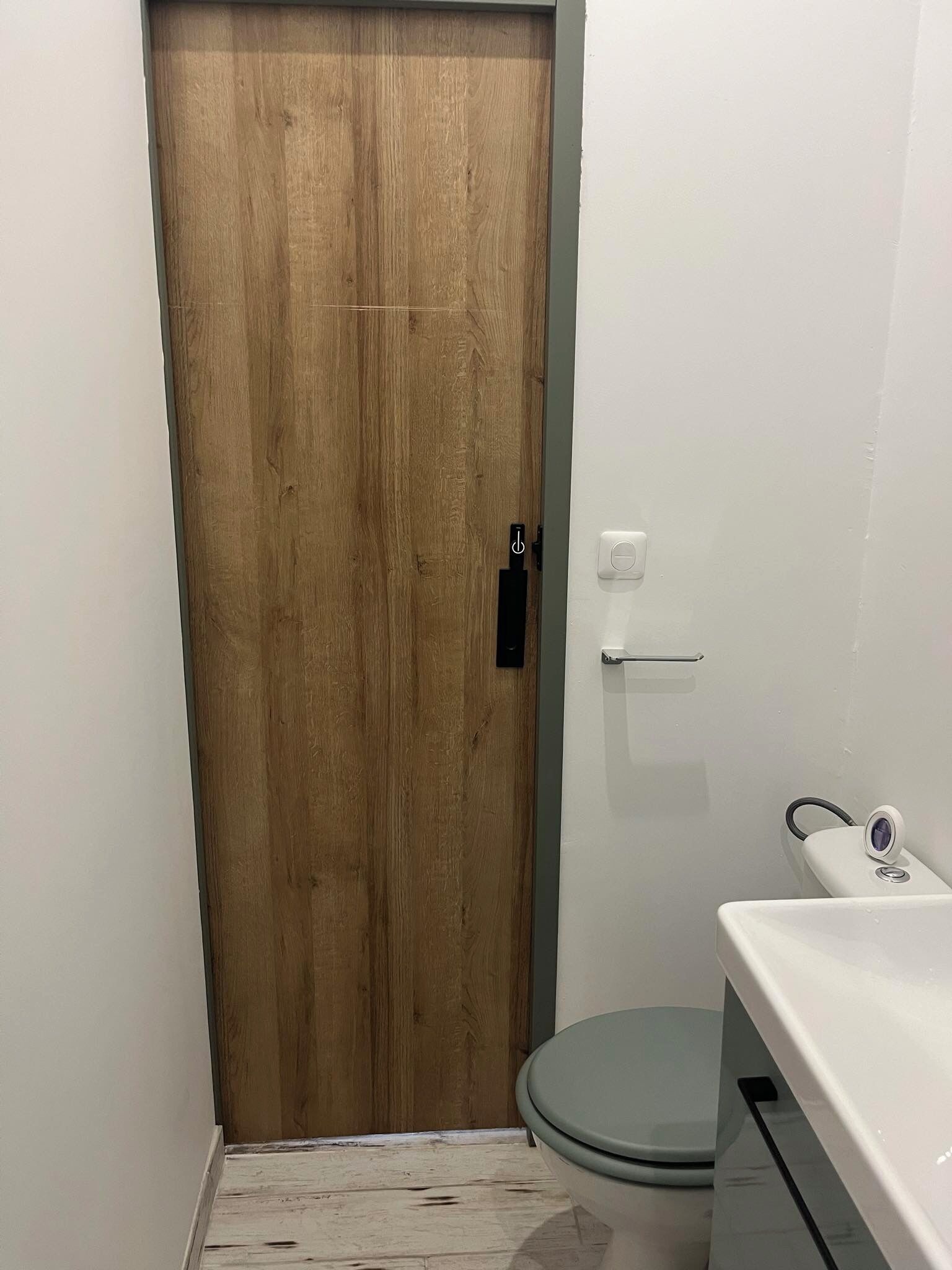 Un baño pequeño con una puerta de madera, un lavamanos blanco y un inodoro.