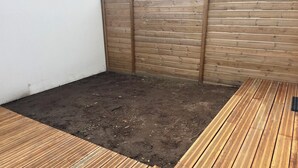 Un petit espace extérieur doté d’une terrasse en bois et d’un coin de terre nue.