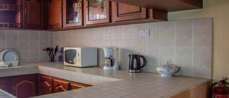 A kitchen with wooden cabinets, a microwave, a coffee maker, and a kettle on the countertop.
