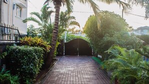 A paved pathway leading to a covered entrance, surrounded by lush greenery and palm trees. - Villa Nass (Flic-en-Flac)