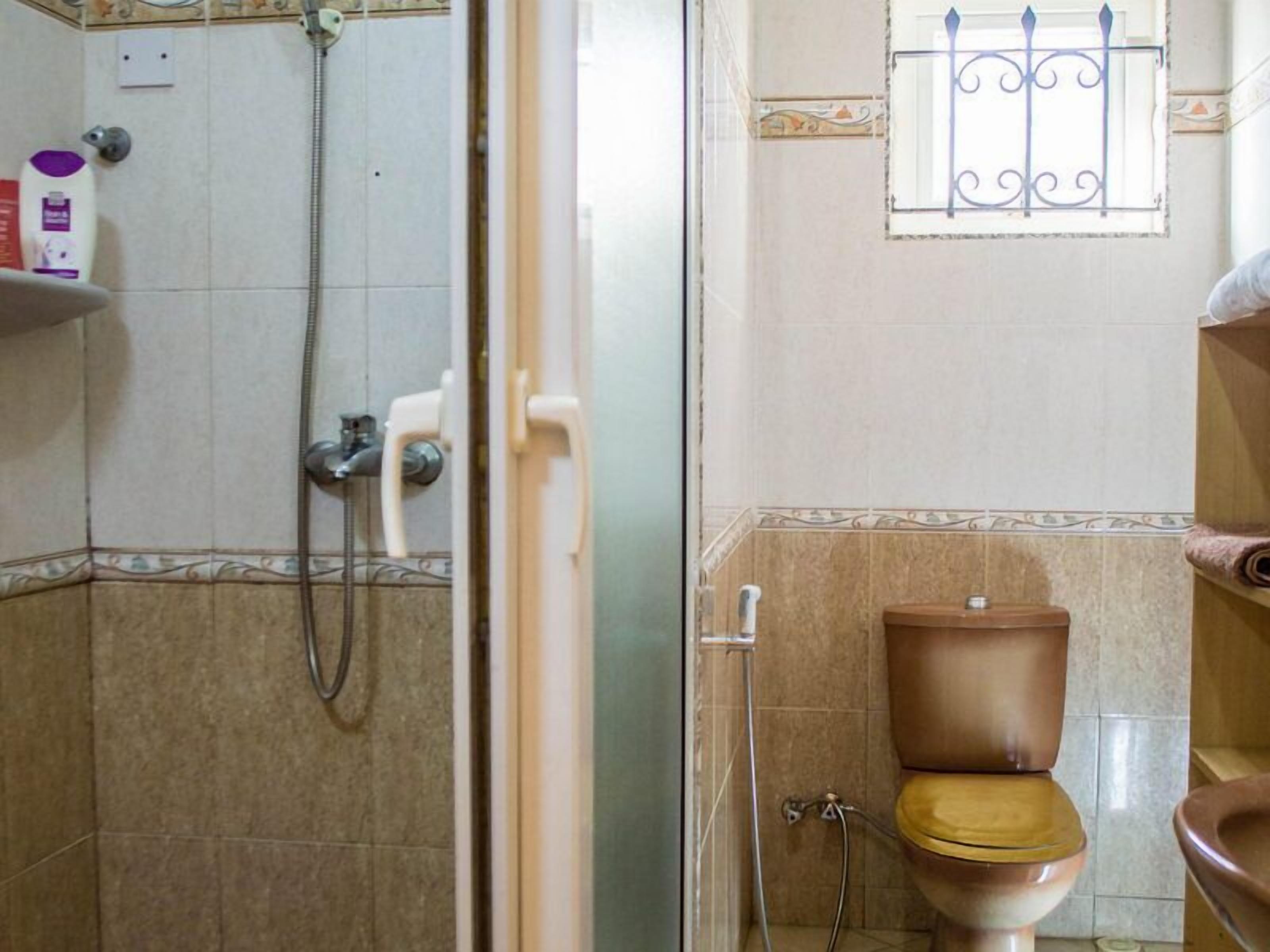 A bathroom with a shower, toilet, and a window with decorative bars.
