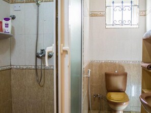 A bathroom with a shower, toilet, and a window with decorative bars. - Villa Nass (Flic-en-Flac)