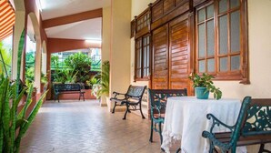 A covered patio area with tiled flooring, wooden furniture, and potted plants. - Villa Nass (Flic-en-Flac)
