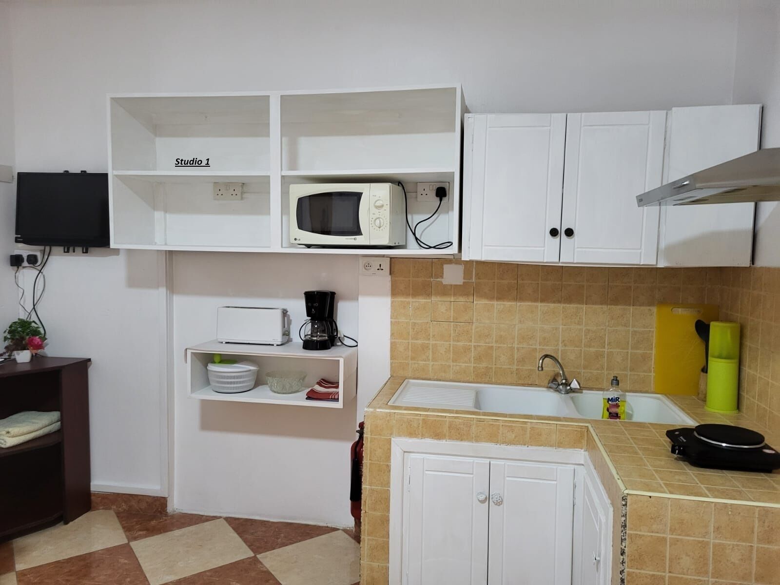 Una cocina compacta con gabinetes blancos, microondas, cafetera y pileta.
