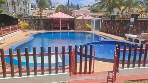 A swimming pool with a red fence, a covered seating area, and a stone wall. - Villa Nass (Flic-en-Flac)