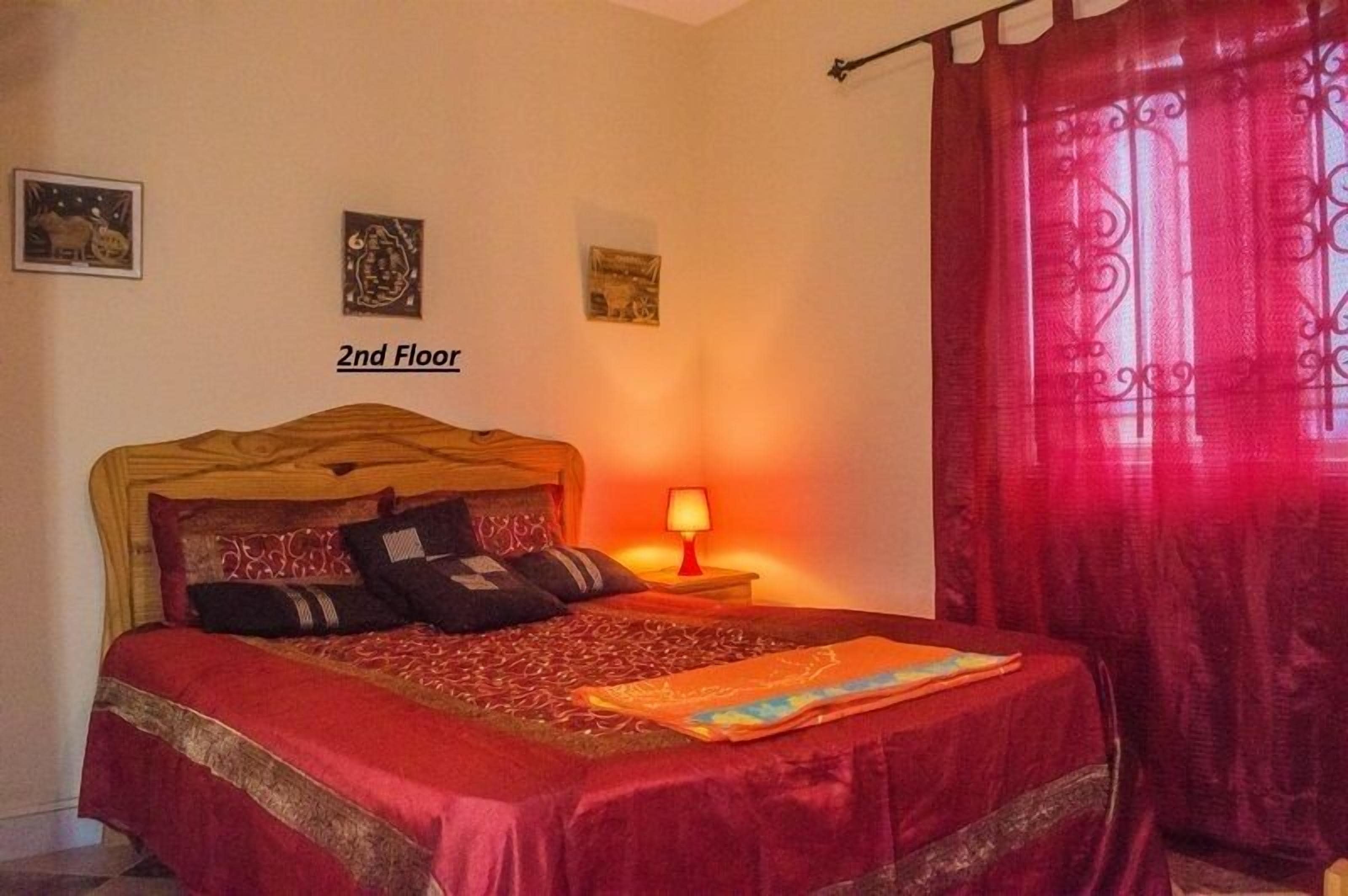 Un dormitorio con una cama, una mesita de noche con una lámpara y una cortina roja.