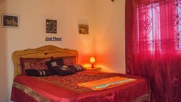 Un dormitorio con una cama, una mesita de noche con una lámpara y una cortina roja.