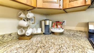 A kitchen with granite countertops, wooden cabinets, a coffee maker, and a mug rack.
