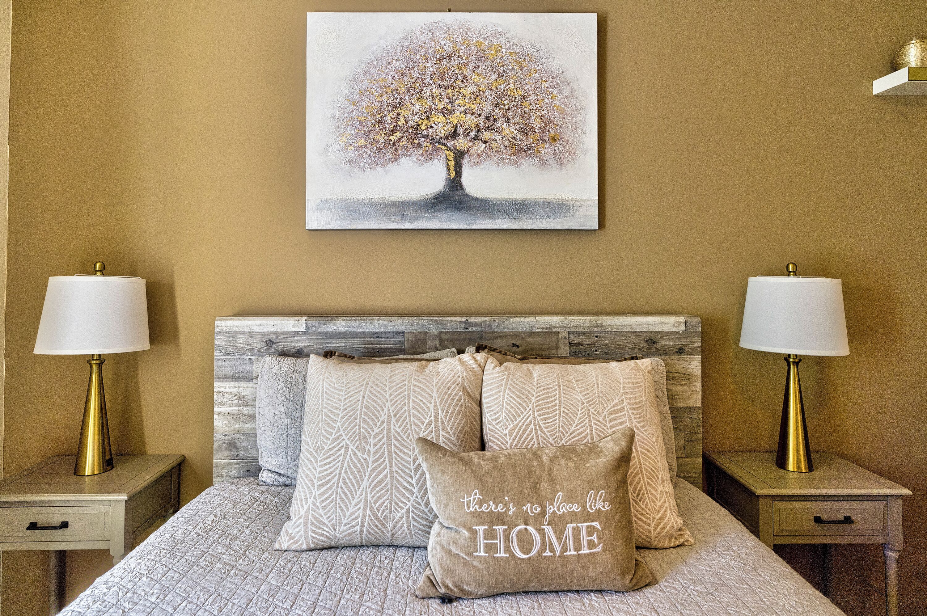 Een slaapkamer met een bed, twee nachtkastjes, twee lampen, een hoofdbord en een schilderij van een boom.