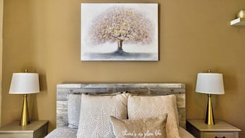 Een slaapkamer met een bed, twee nachtkastjes, twee lampen, een hoofdbord en een schilderij van een boom.
